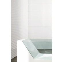 Moderne Badewanne mit Glasseitenwand vor weiß gefliestem Hintergrund.