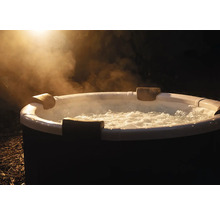 Spa gonflable rond avec eau bouillonnante, appuie-tête et vapeur montante en extérieur de nuit.
