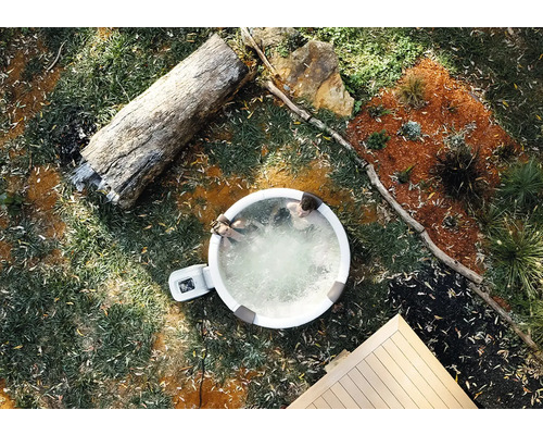 Spa gonflable dans le jardin vue de dessus avec deux personnes, tronc d'arbre et terrasse en bois.