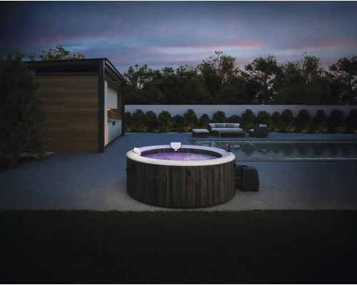 Spa gonflable Intex avec aspect pierre sur une terrasse moderne avec piscine et meubles de jardin au crépuscule.