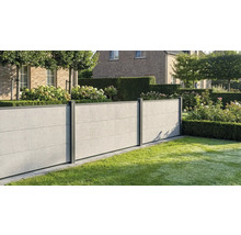 Moderner Sichtschutzzaun in Betonoptik mit dunklen Pfosten in einem gepflegten Garten mit Rasen, Hecken und Hortensien vor einem Backsteinhaus.