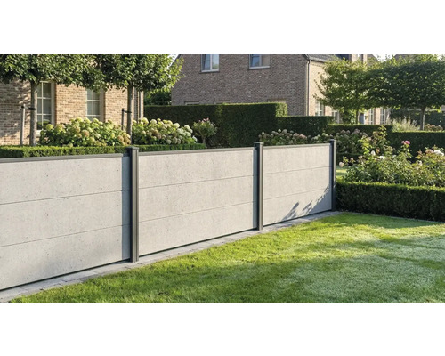 Moderner Sichtschutzzaun in Betonoptik mit dunklen Pfosten in einem gepflegten Garten mit Rasen, Hecken und Hortensien vor einem Backsteinhaus.