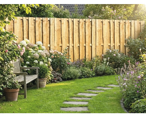 Ein gepflegter Garten mit einem Sichtschutzzaun aus Naturholzbrettern, einer Holzbank, Blumenbeeten mit Hortensien und einem Trittsteinpfad im Rasen.