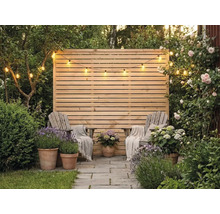 Paravent en bois à lattes horizontales, deux chaises en bois avec couvertures, pots en terre cuite avec lavande et hortensias et une guirlande lumineuse.