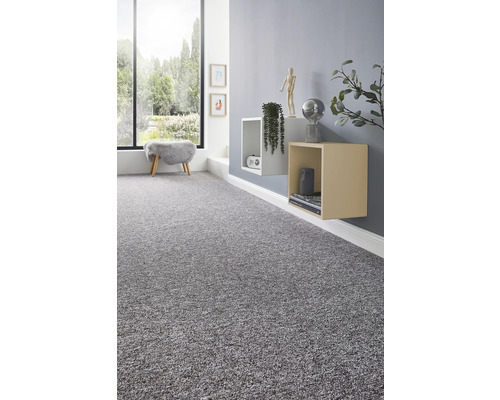 Moquette grise texturée dans une pièce moderne et lumineuse avec une grande fenêtre et des étagères murales cubiques.