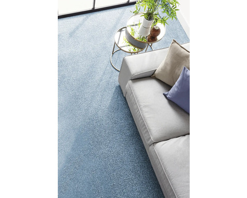 Moquette bleue texturée dans un salon lumineux avec un canapé gris et une table d'appoint en verre.