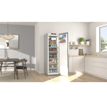 Congélateur armoire ouvert rempli de nourriture dans une cuisine moderne et lumineuse avec table à manger et meubles blancs.