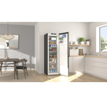 Congélateur armoire ouvert rempli de produits alimentaires dans une cuisine moderne et lumineuse avec un coin repas.