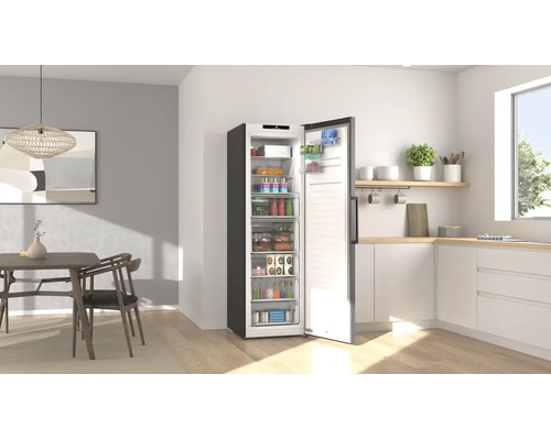 Congélateur armoire ouvert rempli de produits alimentaires dans une cuisine moderne et lumineuse avec un coin repas.