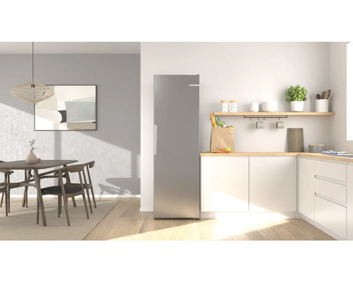 Réfrigérateur pose libre moderne en aspect inox dans une cuisine lumineuse et organisée avec coin repas et éléments en bois.
