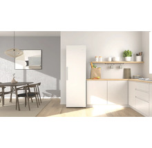 Cuisine moderne et lumineuse avec un réfrigérateur blanc indépendant, des plans de travail en bois et un coin repas avec des meubles en bois.