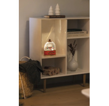 Beleuchtete Schneekugel mit Winterszene in einem weißen Regal neben einer Vase, Büchern und einem Geschenkpaket.