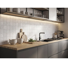 Cuisine moderne avec plan de travail en bois, meubles sombres, carreaux muraux carrés, robinet noir et éclairage sous les étagères.