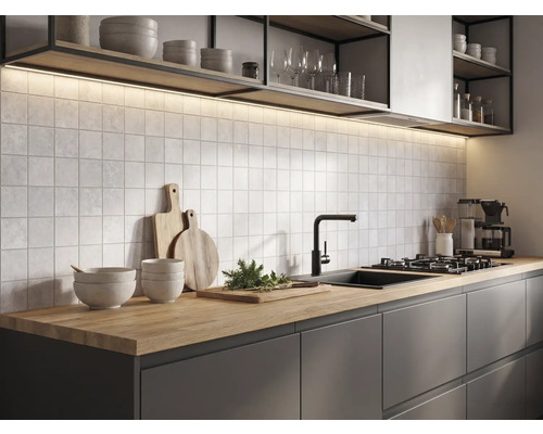Cuisine moderne avec plan de travail en bois, meubles sombres, carreaux muraux carrés, robinet noir et éclairage sous les étagères.