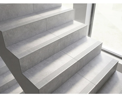 Escalier avec carrelage aspect pierre et rainures antidérapantes sur les marches.