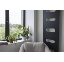 Intérieur moderne avec radiateur design vertical noir, plantes vertes à la fenêtre et fauteuil gris.