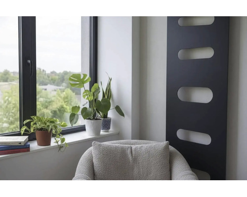 Intérieur moderne avec radiateur design vertical noir, plantes vertes à la fenêtre et fauteuil gris.