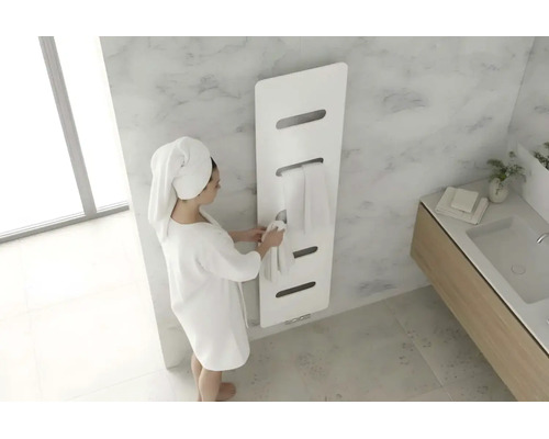 Sèche-serviettes moderne blanc dans une salle de bains lumineuse avec aspect marbre et une personne en peignoir.