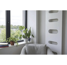 Espace de vie lumineux avec radiateur moderne, fauteuil et plantes d'intérieur sur le rebord d'une fenêtre à cadre noir.
