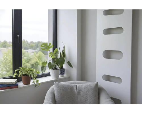 Espace de vie lumineux avec radiateur moderne, fauteuil et plantes d'intérieur sur le rebord d'une fenêtre à cadre noir.