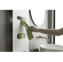 Une main retire une serviette verte d'un radiateur design blanc dans une salle de bains moderne avec vasque et robinet.