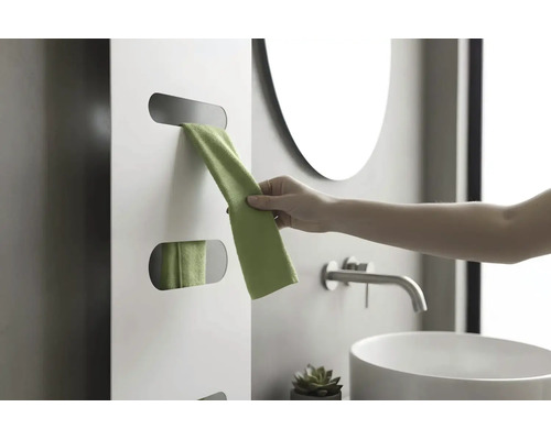 Une main retire une serviette verte d'un radiateur design blanc dans une salle de bains moderne avec vasque et robinet.