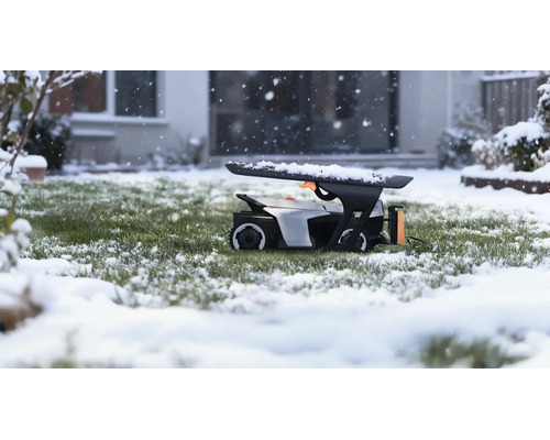 Mähroboter in einer Roboter-Garage auf einer verschneiten Rasenfläche während Schneefall vor einem Haus.