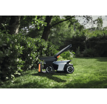 Mähroboter mit Zubehör auf einer Rasenfläche im Garten neben einer Hecke.