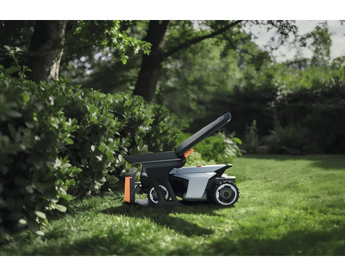 Mähroboter mit Zubehör auf einer Rasenfläche im Garten neben einer Hecke.