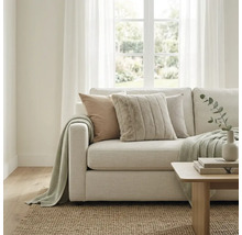 Helles Wohnzimmer mit modernem Stoffsofa, strukturierten Kissen und Strickdecke. Ein Juteteppich und ein Holztisch ergänzen den Raum.