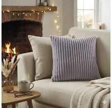 Coussin décoratif lavande à texture côtelée sur un canapé clair dans un salon chaleureux avec cheminée allumée et table d'appoint.