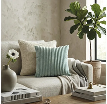 Salon moderne avec un coussin en velours côtelé vert menthe et un coussin en tricot beige sur un canapé en tissu neutre.