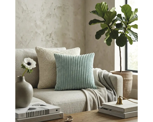 Salon moderne avec un coussin en velours côtelé vert menthe et un coussin en tricot beige sur un canapé en tissu neutre.