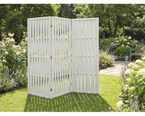 Paravent de jardin en bois blanc à trois panneaux sur une pelouse au milieu d'un jardin fleuri.