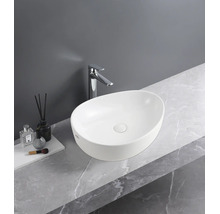 Vasque à poser ovale blanche sur un plan de travail aspect marbre avec robinetterie chromée.