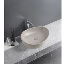 Vasque à poser ovale beige mat sur un plan de travail aspect marbre avec robinetterie chromée.