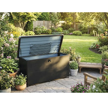Coffre de jardin en métal avec couvercle ouvert et filet de rangement sur une terrasse pavée dans un jardin avec des plantes et des fleurs.