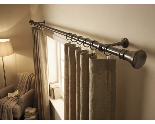 Tringle à rideaux en métal avec anneaux et rideaux en tissu dans une pièce lumineuse avec fenêtre et fauteuil.