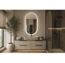 Salle de bain moderne avec miroir LED ovale, vasque à poser striée, meuble sous-vasque clair et douche à l'italienne aspect marbre.