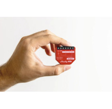 Eine Hand hält das kompakte Shelly Gen3 WLAN-Relais in Rot zur Veranschaulichung der geringen Größe für die Unterputzmontage.