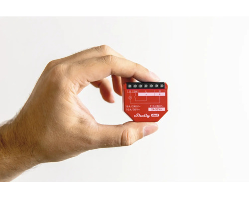 Eine Hand hält das kompakte Shelly Gen3 WLAN-Relais in Rot zur Veranschaulichung der geringen Größe für die Unterputzmontage.
