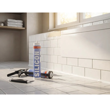 Silikonkartusche mit Kartuschenpistole und Fugenglätter in einem hellen Badezimmer vor einer gefliesten Badewanne.