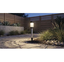 Lampe solaire dans un jardin sur un chemin en pierre à côté de graminées et d'une clôture en bois au crépuscule.