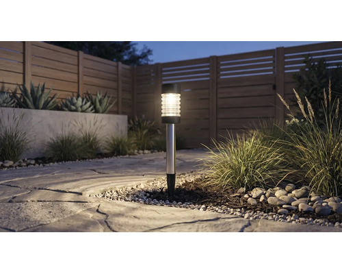Lampe solaire dans un jardin sur un chemin en pierre à côté de graminées et d'une clôture en bois au crépuscule.