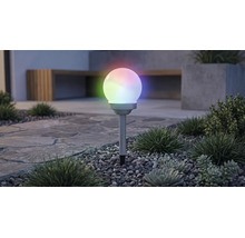 Lampe solaire de jardin en forme de boule avec éclairage RGB multicolore, sur un piquet dans un parterre de gravier avec des plantes.