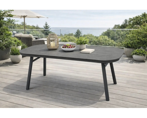 Table de jardin ovale moderne sur une terrasse en bois. La table sombre est décorée avec une lanterne, un bol de fruits et une plante.