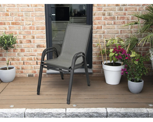 Chaise de jardin empilable avec cadre en aluminium et revêtement textile sur une terrasse en bois avec des plantes devant un mur en briques.