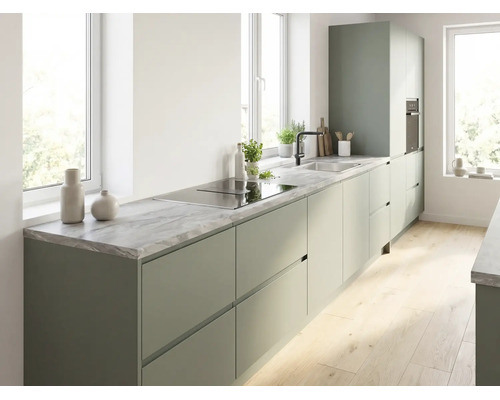 Cuisine moderne avec meubles vert mat sans poignées, plan de travail aspect marbre, plaque de cuisson intégrée et évier sous lumière naturelle.