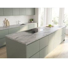 Cuisine moderne lumineuse avec îlot, meubles vert sauge, plan de travail aspect marbre et crédence en carrelage blanc.