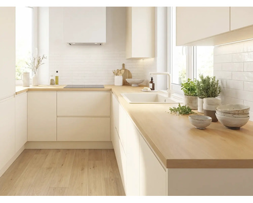 Cuisine moderne en L avec façades sans poignées claires, plan de travail en bois, crédence blanche, évier et plaque à induction.